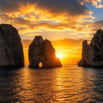 Sunset over sea with three large rock formations and glowing clouds.