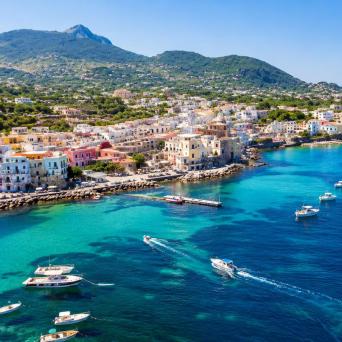 Aerial view of a coastal town with colorful buildings, docked boats, and clear blue waters.