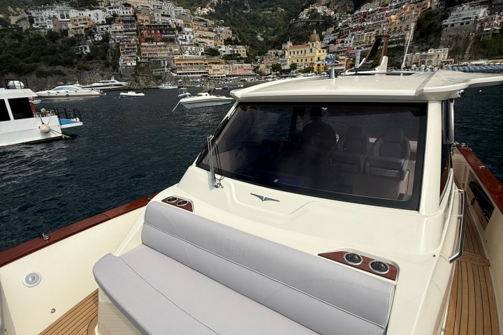 Luxury boat with town and mountains in background, sunny day.