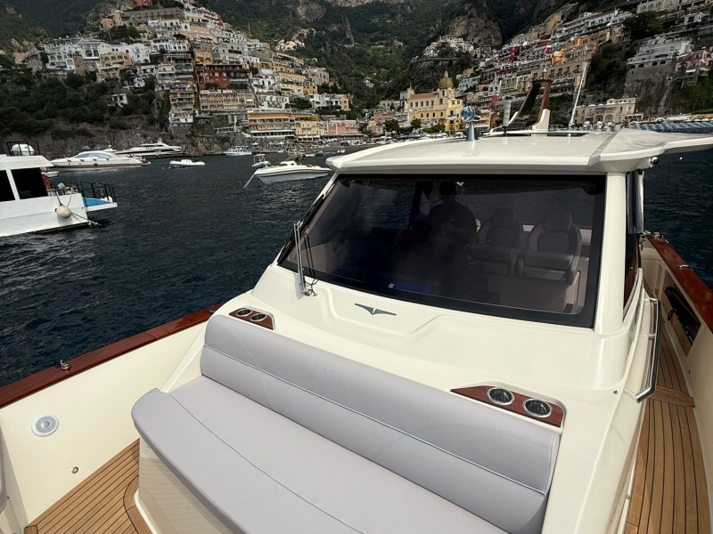 Luxury boat with town and mountains in background, sunny day.