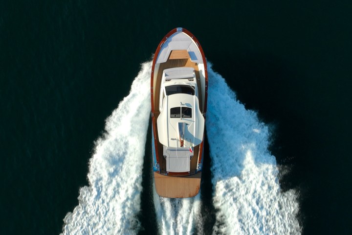 Overhead view of a yacht moving through dark water, creating white waves.